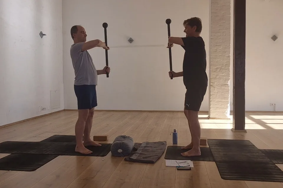 Zwei Übende stehen einander gegenüber und halten den Steel Mace senkrecht vor dem Körper